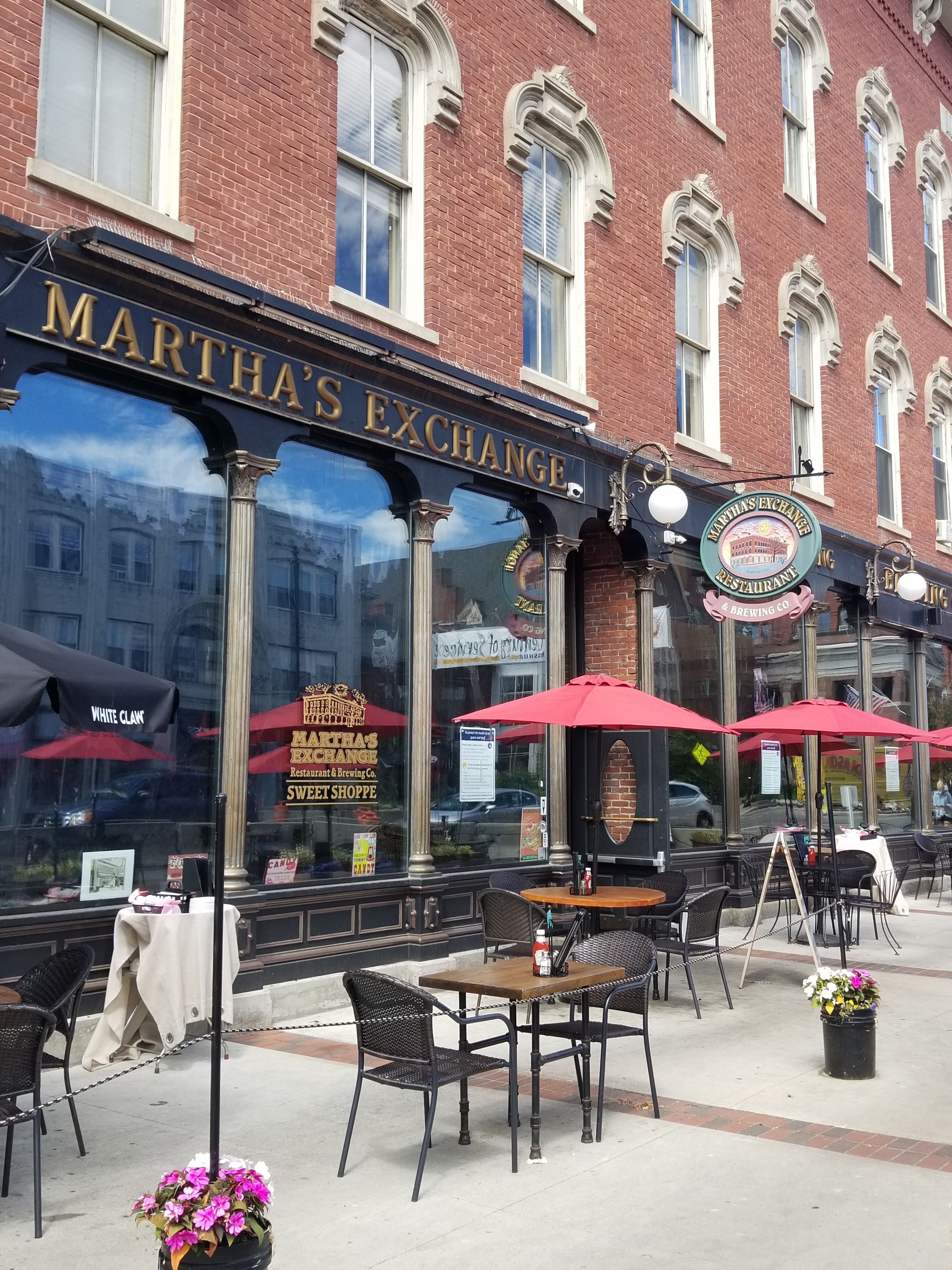 This is a photo of Martha's Exchange and the sidewalk outside the establishment, which contains tables, chairs, umbrellas, and small flower pots that connect a partition separating the area from the rest of the New Hampshire sidewalk, presented by Nashua personal injury lawyer Attorney Buckley